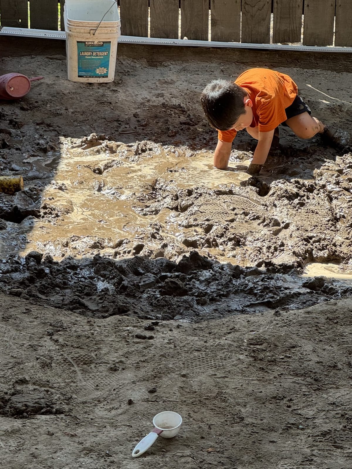 Young child exploring a muddy puddle with hands and feet