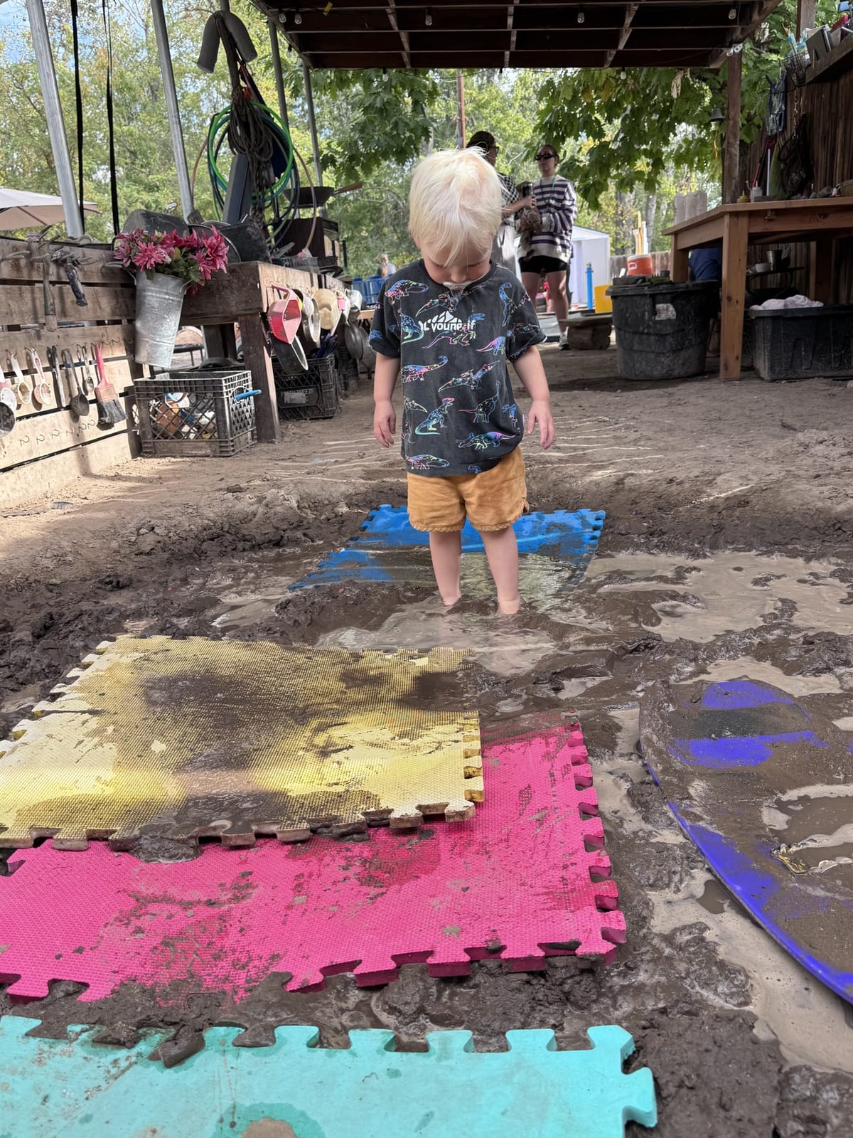 Young child walking across colorful play mats beside a puddle