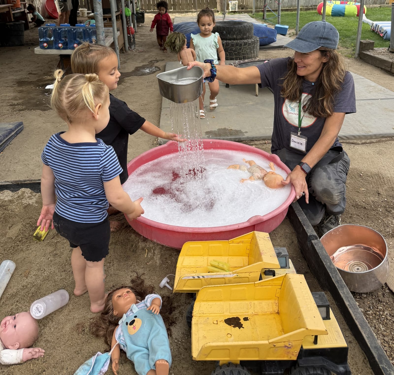 Young children exploring water and bubbles with an adult at the outdoor play table