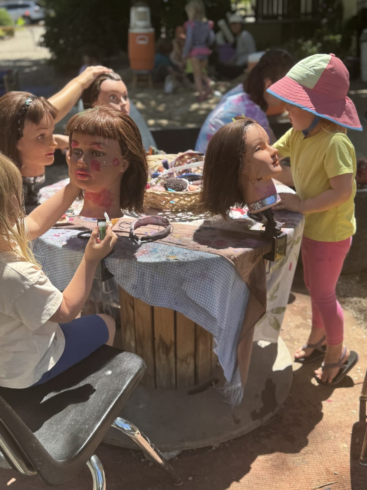 Children styling mannequin heads together at an outdoor imaginative-play table