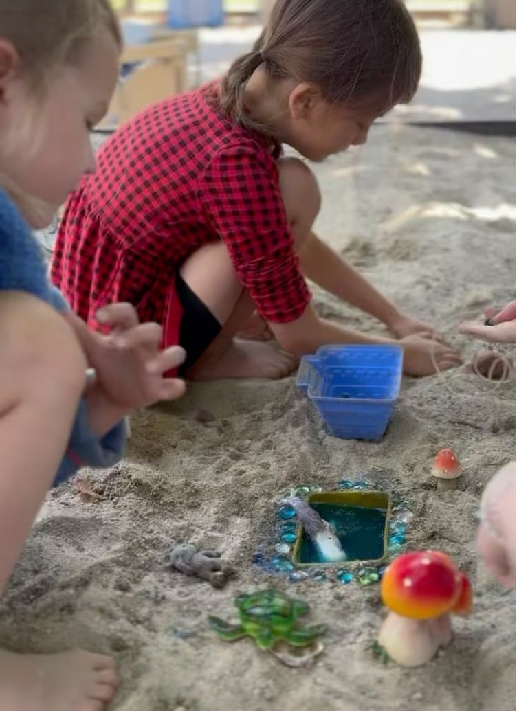 Children exploring sand and small loose-parts play materials together