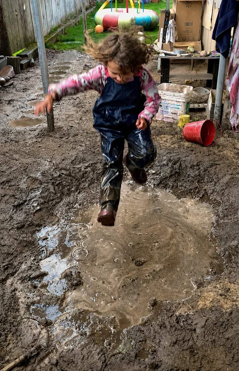 A child jumping through a puddle at the mud kitchen